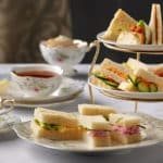An assortment of delicate finger sandwiches is elegantly arranged on a three-tiered porcelain stand